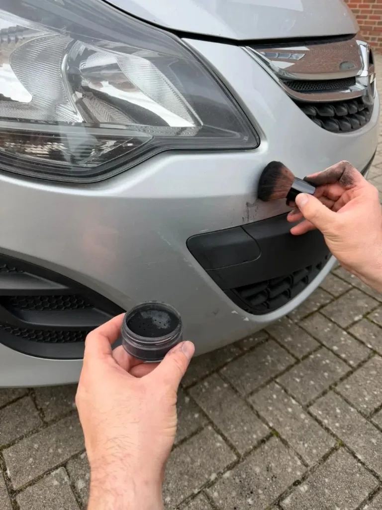 Kontaktpuder wird mit einem Pinsel auf den Stoßfänger eines silbernen Autos aufgetragen