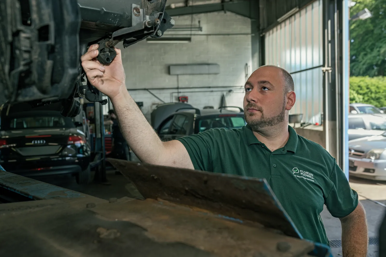 Florian Pudwell prüft auf der Hebebühne ein Bauteil am Unterboden eines Fahrzeugs